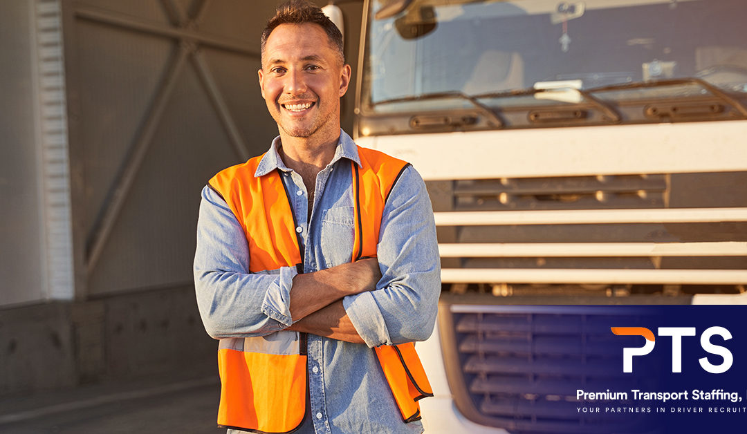 A smiling male truck driver with his arms crossed, standing in front of a parked truck