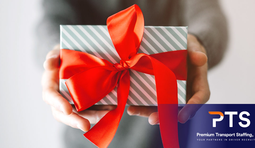 A close up of a pair of hands giving a small boxed gift with a big red bow