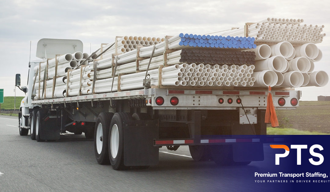 The rear view of a flat bed truck hauling a load of pipes of varying sizes